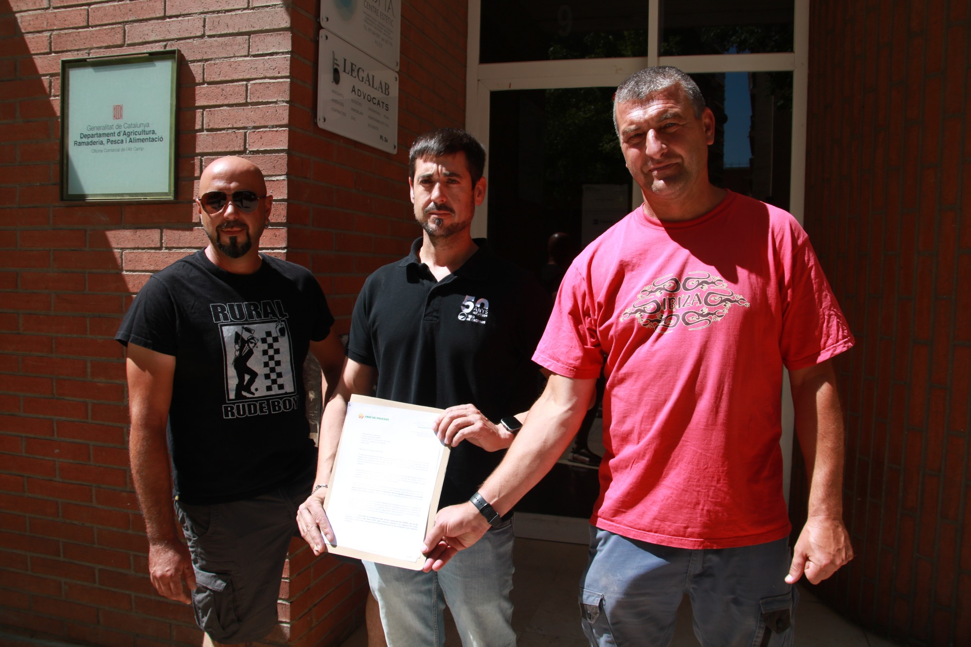 El responsable de la Vinya i el Vi d'Unió de Pagesos, David Sendra, acompanyat de dos pagesos a l'entrada de les oficines comarcals d'Agricultura abans de lliura la carta per demanar que impulsi l'arrencada de les vinyes i que se'n faci un recompte